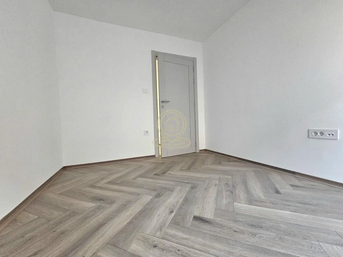 Prazna prostorija sa belim zidovima i drvenim podom.