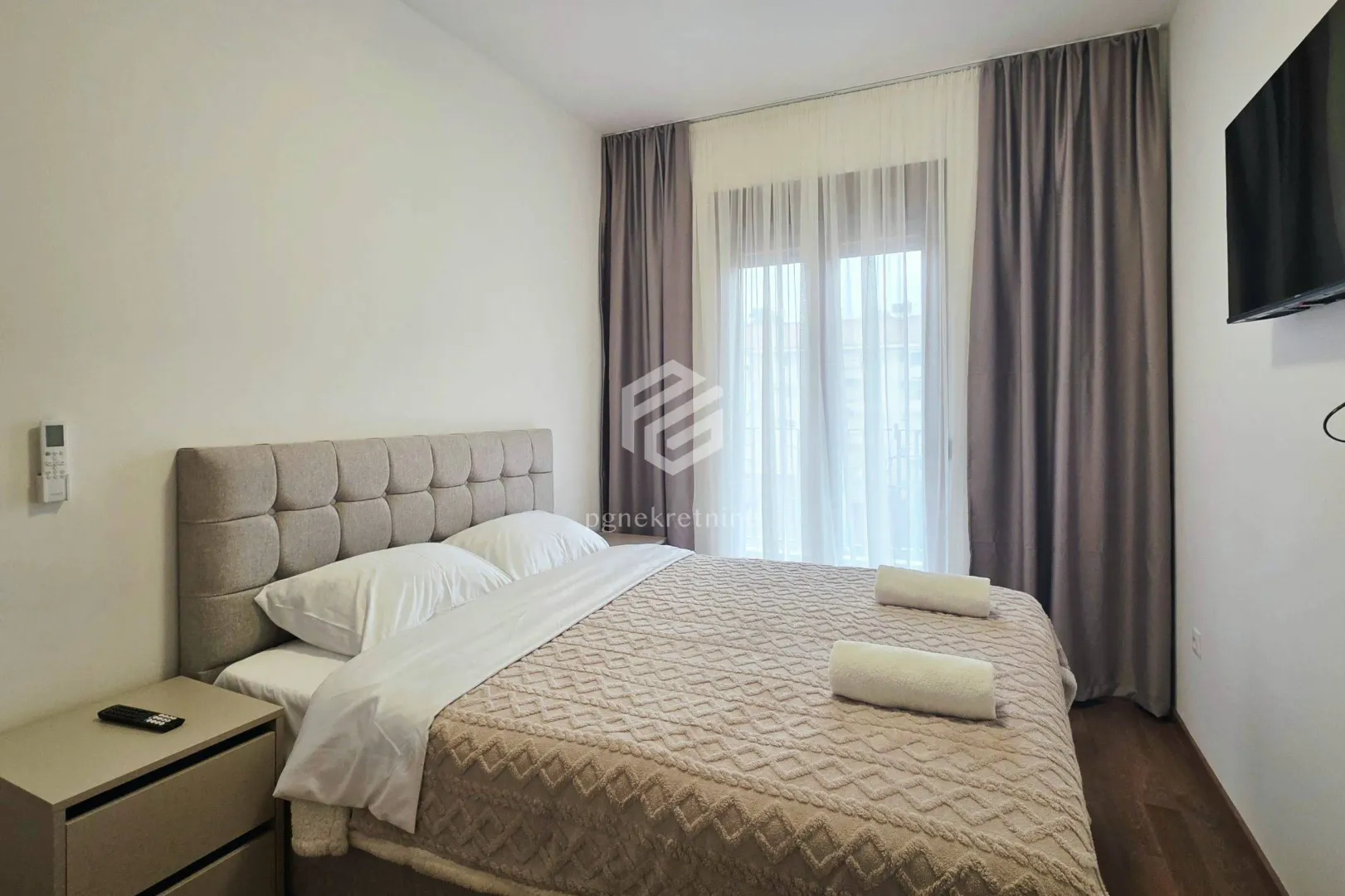 Furnished bedroom with a double bed, nightstand and wall-mounted TV.
