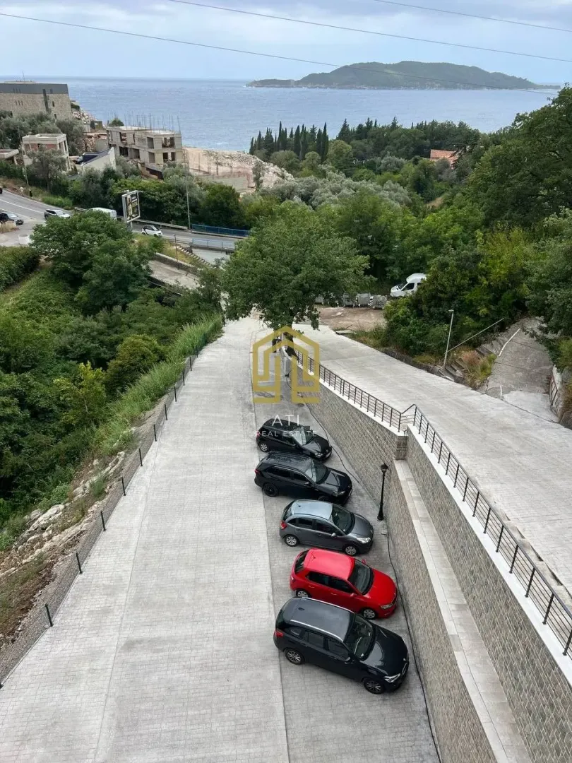 Pogled sa terase na parking prostor i more u daljini.