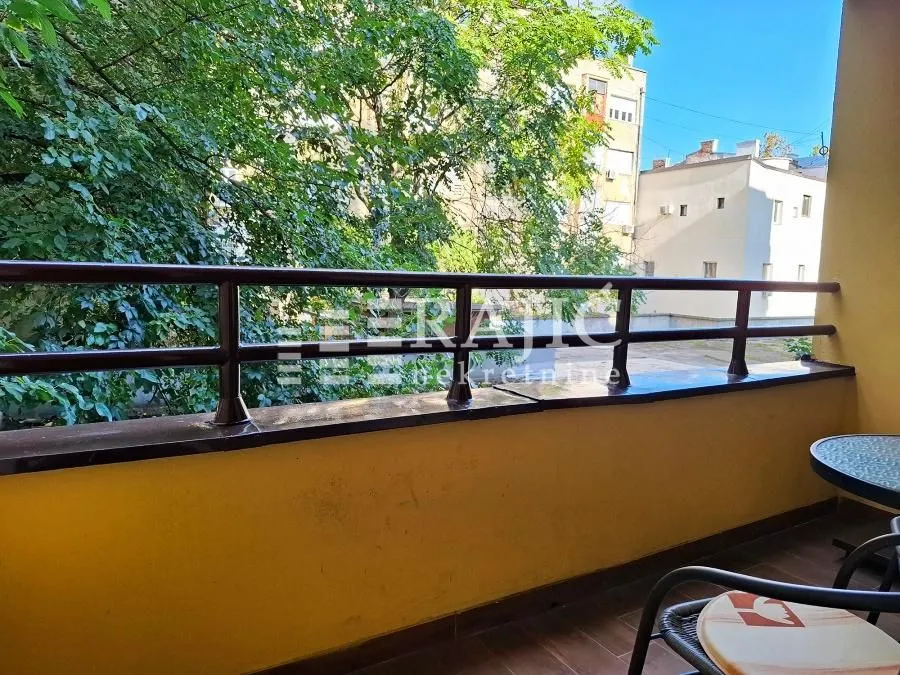 Small furnished balcony with a view of surrounding buildings and greenery.