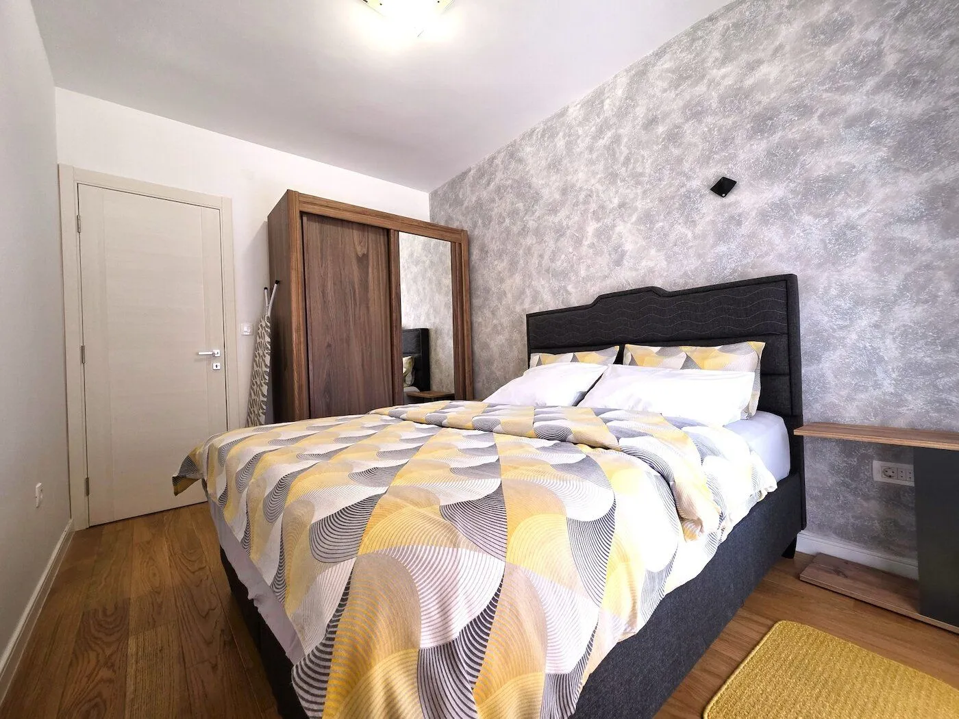 Furnished bedroom with a double bed, wooden wardrobe, and laminate flooring.