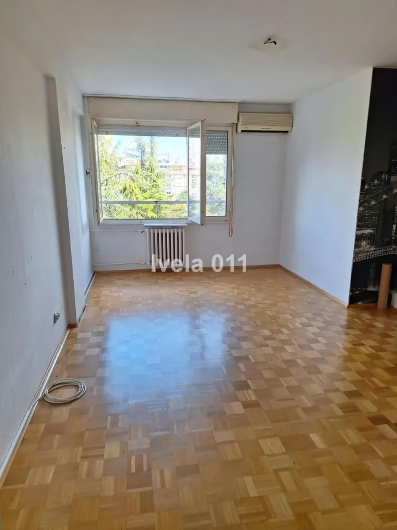Empty room with parquet flooring and a window overlooking greenery.