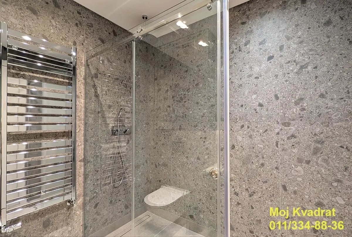 Modernly equipped bathroom with a walk-in shower and grey tiles.