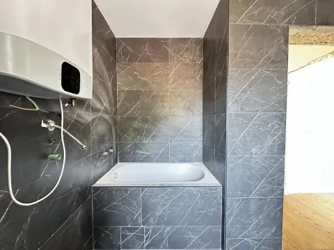 Kupatilo u fazi opremanja sa ugrađenom kadom i tamnim pločicama. - image 6