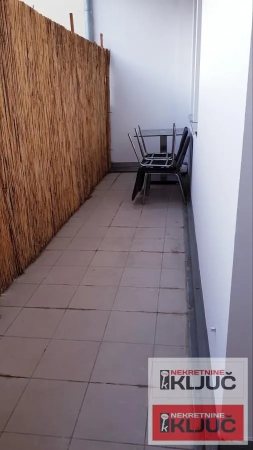 Uski popločani balkon sa ogradom od trske i složenim stolicama.