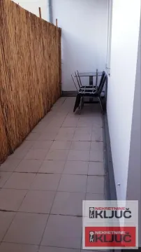 Uski popločani balkon sa ogradom od trske i složenim stolicama. - image 6