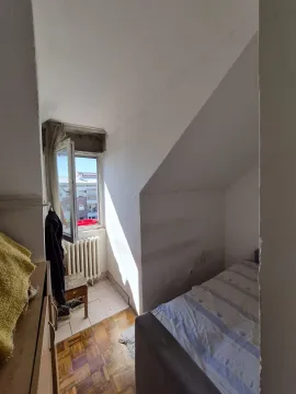 Manja spavaća soba sa krevetom i prozorom koji gleda na grad. - image 7