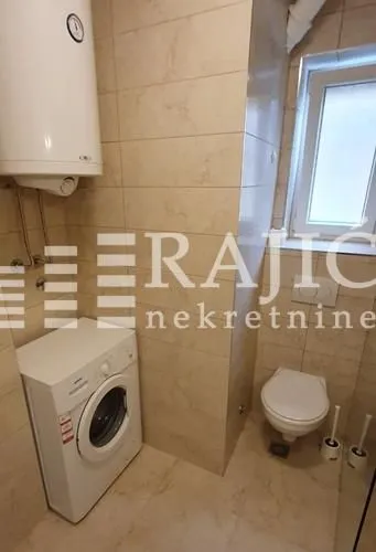 Smaller bathroom tiled with ceramic tiles featuring a toilet, washing machine, and water heater.