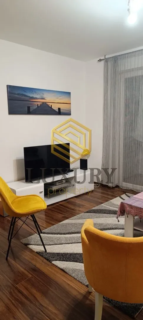 Dnevna soba sa garniturom, televizorom i trpezarijskim stolom.