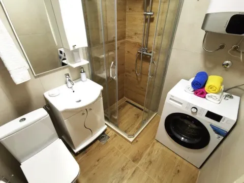 Small bathroom with a shower cabin, sink, toilet, and washing machine. - image 13