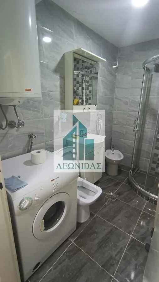 Modernly equipped bathroom with a shower cabin, washbasin, and washing machine.