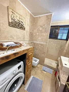 A stone-tiled bathroom with a washing machine and sink. - image 11