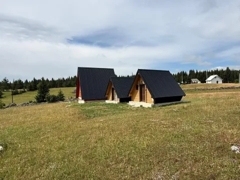 Drvene vikendice sa crnim krovovima okružene livadom i šumom. - image 2
