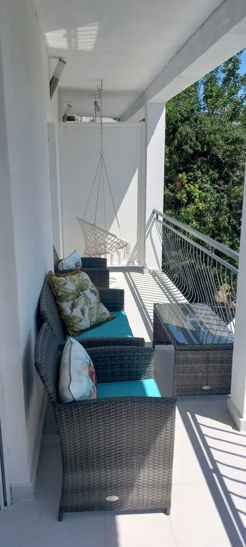 Dugačak natkriveni balkon opremljen garniturom za sjedenje i visećom stolicom.