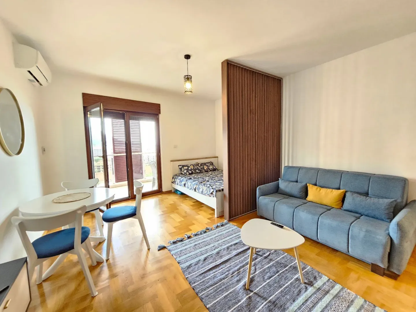 Living room with a sofa set, dining table, and a bed in the background.