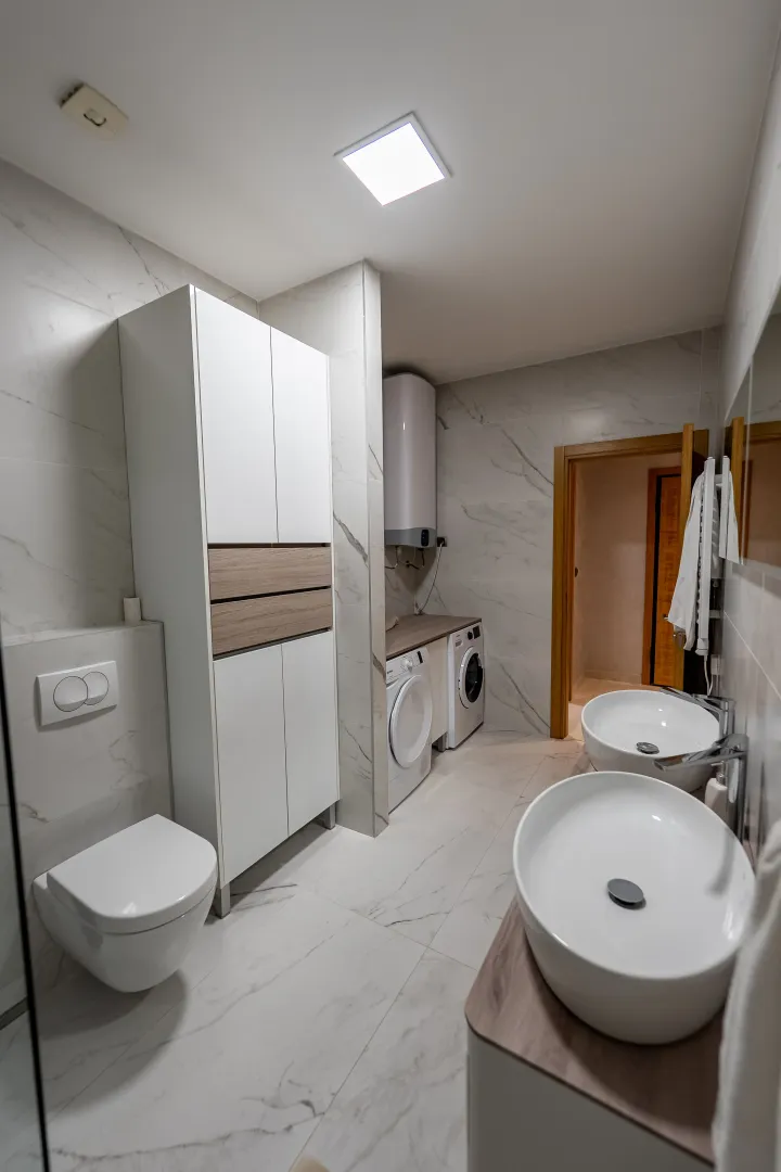Modernly equipped bathroom with two washbasins, a washing machine, and a built-in toilet.