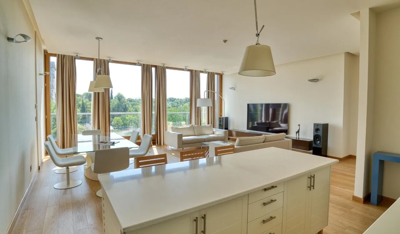 Spacious open-plan living room with a dining area and kitchen island, featuring large windows and nature views.