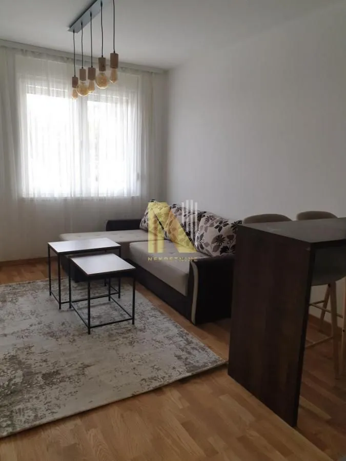 Dnevni boravak sa garniturom, stočićem i prozorom sa belim zavesama.