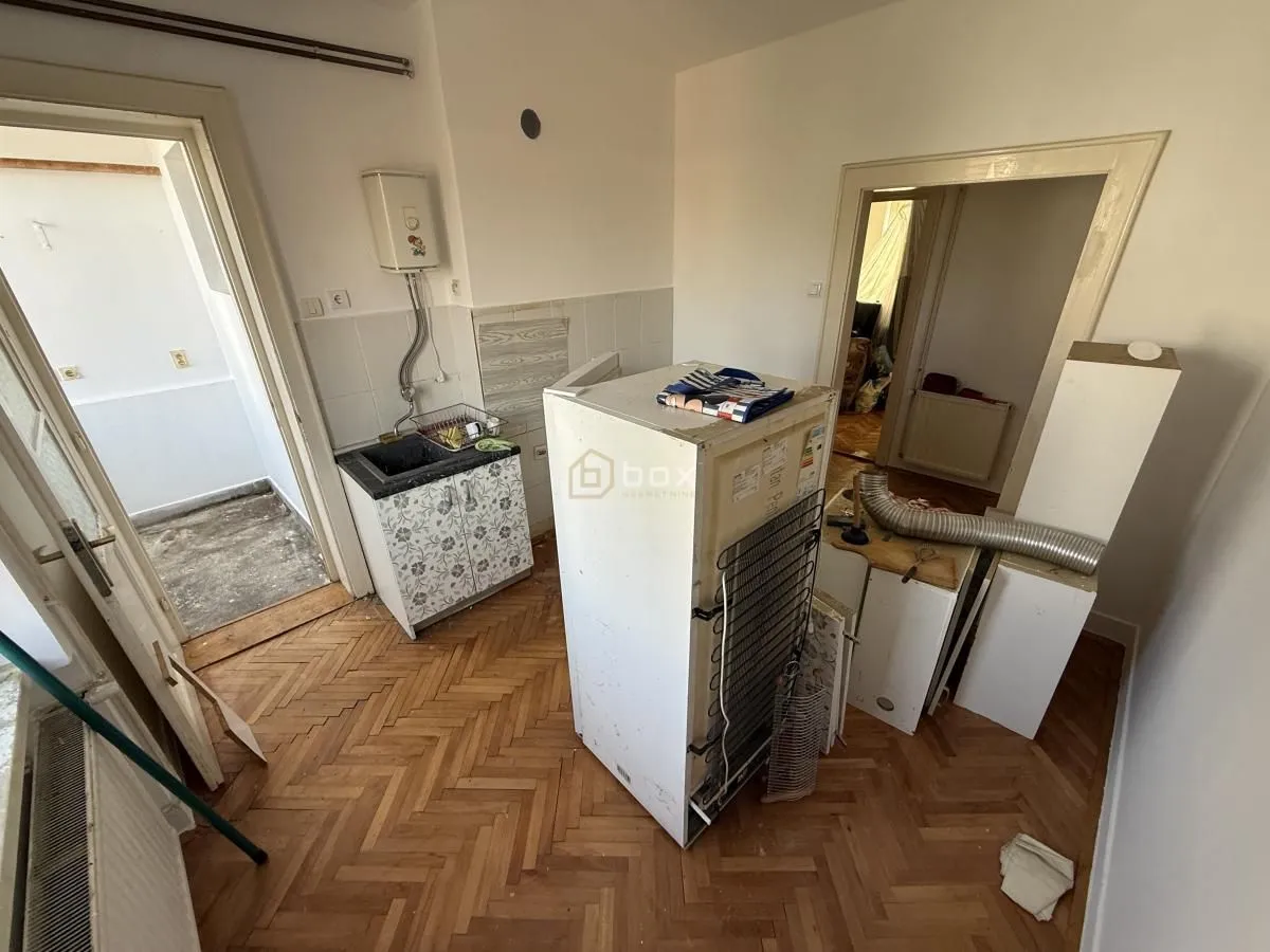 Starija kuhinja sa osnovnim elementima i frižiderom u renoviranju.