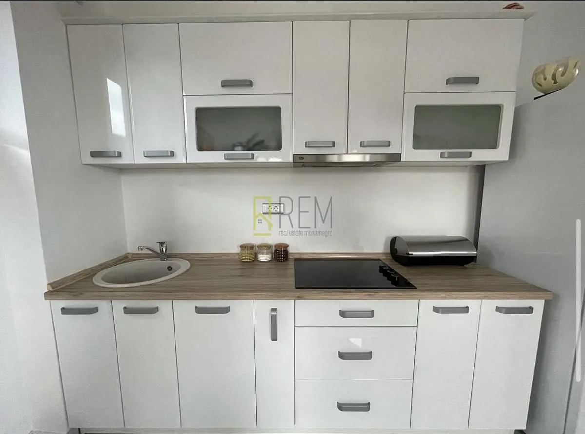 White kitchen with a wooden countertop, sink, and built-in hob.