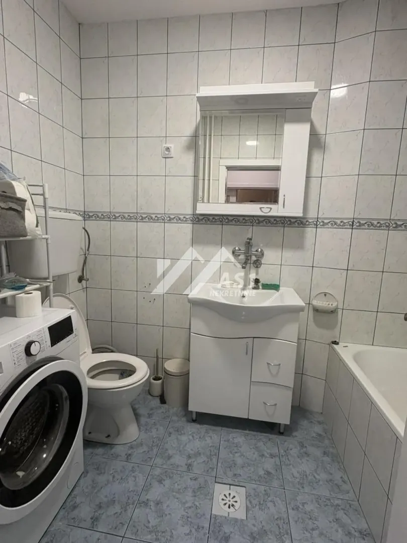Kupatilo opremljeno sanitarijama, umivaonikom sa ormarićem, kadom i veš mašinom.