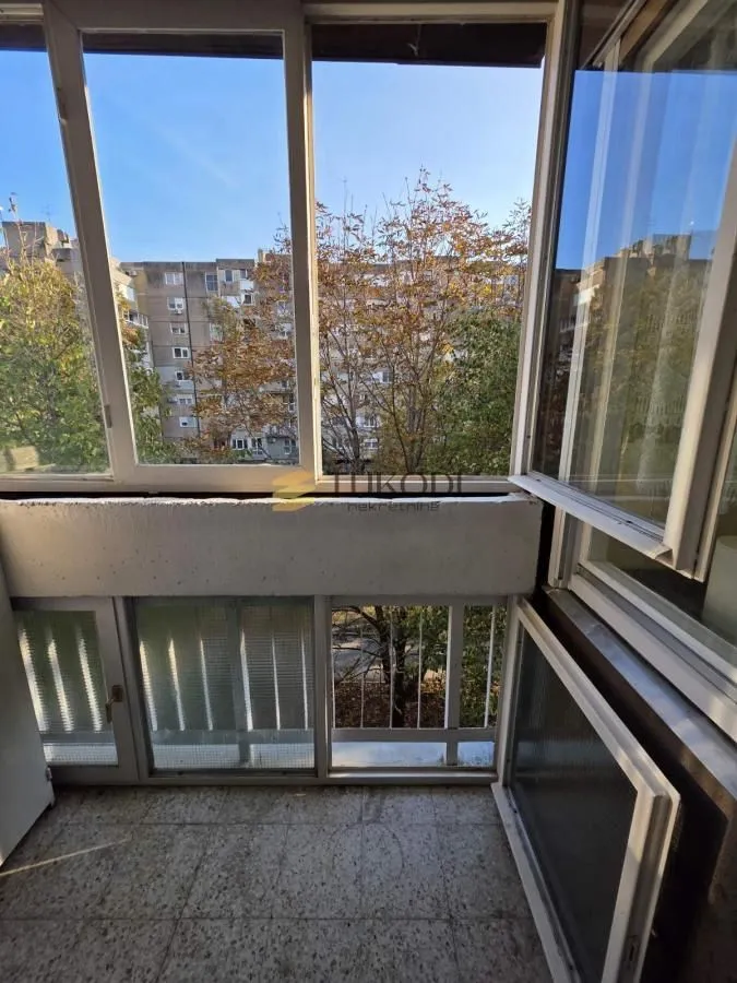 Zastakljeni balkon sa pogledom na susedne zgrade i drveće.