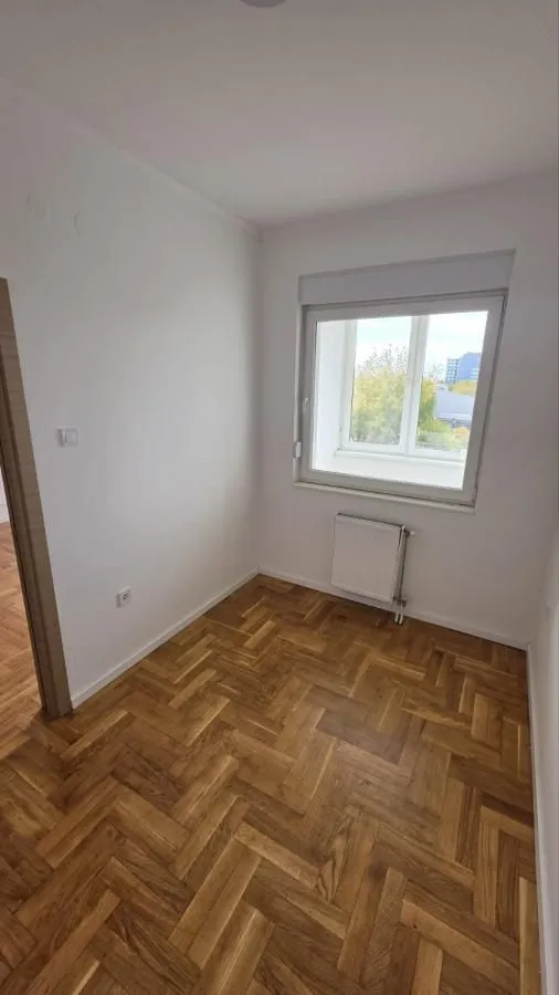 Prazna soba sa parketom i prozorom.