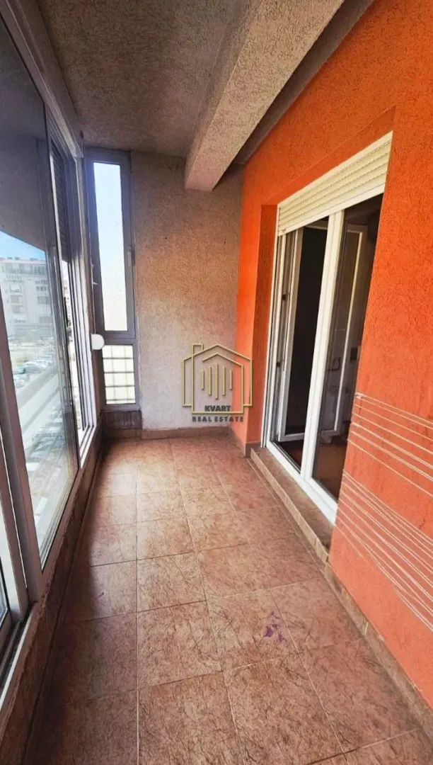 Natkriveni balkon sa popločanim podom i velikim staklenim površinama.