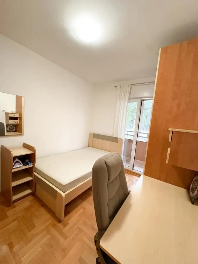 Manja spavaća soba sa krevetom, radnim stolom i izlazom na terasu.