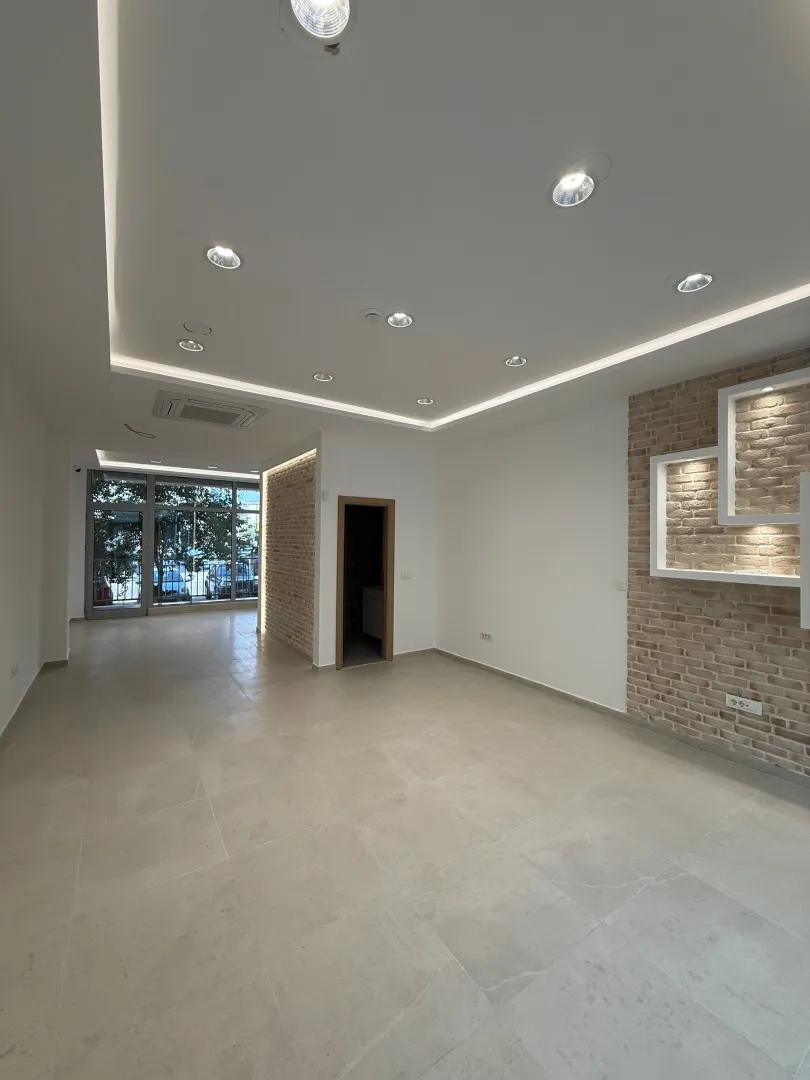 Empty bright living room with dropped ceiling, lighting, and brick accent wall details.