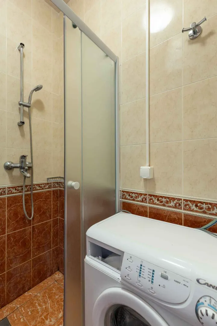 Kupatilo sa tuš kabinom i veš mašinom obloženo keramičkim pločicama.