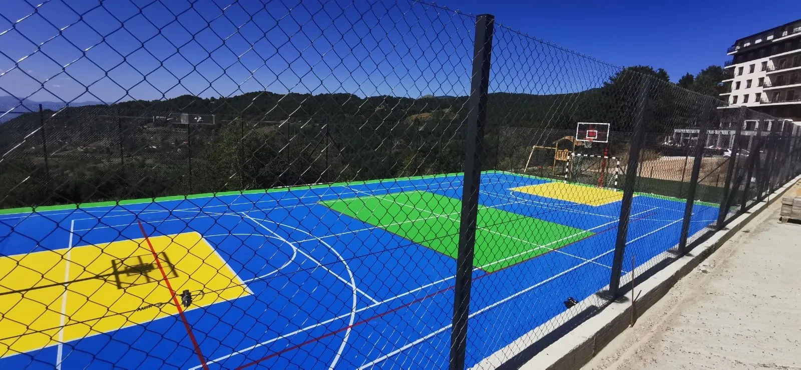 Sportski teren sa veštačkom podlogom i ogradom u okruženju prirode.