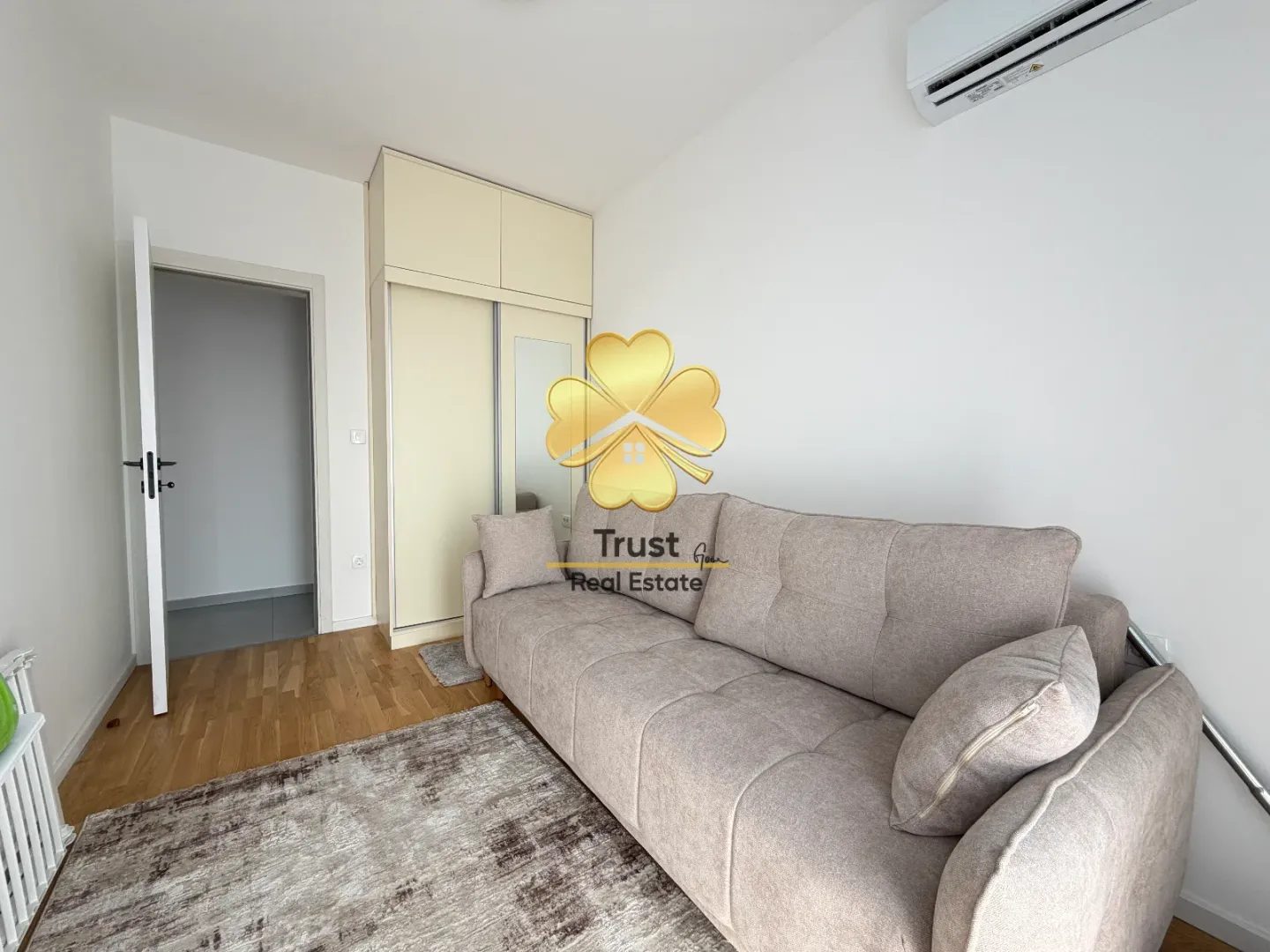 Living room with a beige sofa, wardrobe, and air conditioning unit.