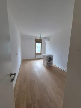 Prazna soba sa drvenim podom i zapakovanom veš mašinom. - image 11