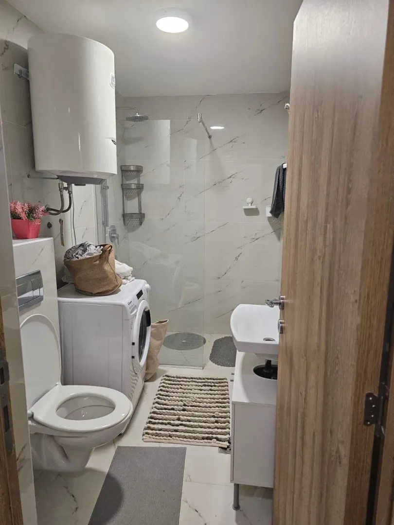 Moderne kupatilo sa tuš kabinom, umivaonikom, WC šoljom i veš mašinom.