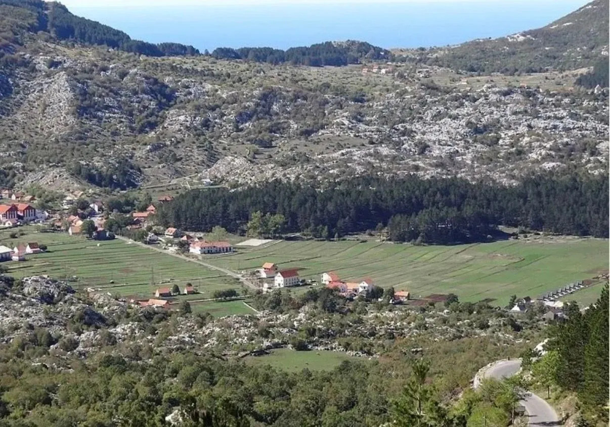 Pogled iz ptičje perspektive na selo u dolini okruženo brdima i zelenilom.