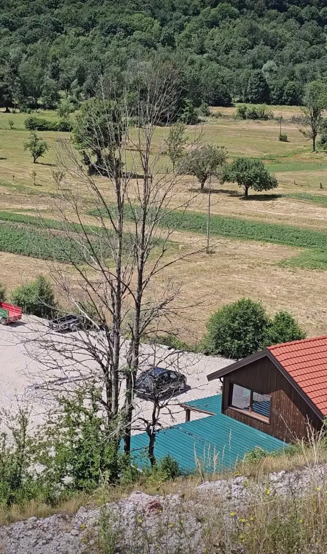 Pogled odozgo na seosko imanje sa kućom i voćnjakom u pozadini.
