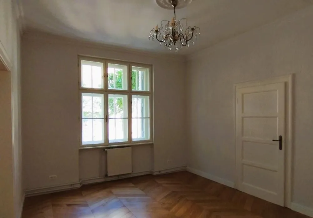 Empty room with a window, wooden parquet flooring, and a chandelier.
