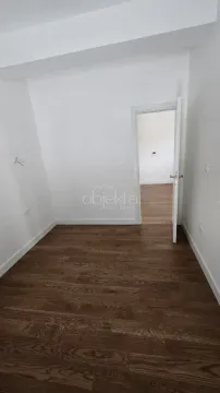 Prazna soba sa bijelim zidovima, tamnim parketom i otvorenim vratima prema drugoj prostoriji. - image 5