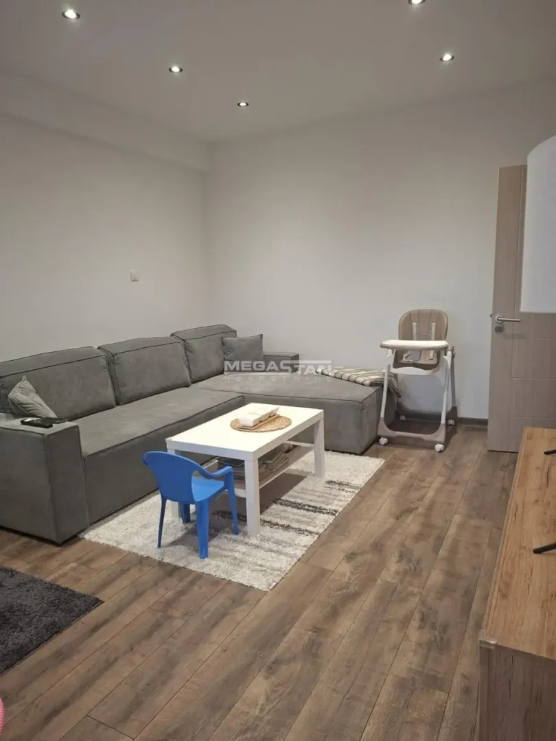 Dnevna soba sa ugaonom garniturom, stočićem i nameštajem od drveta.