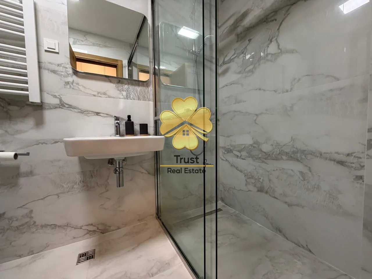 Modern bathroom equipped with marble tiles, a washbasin, and a glass shower cabin.