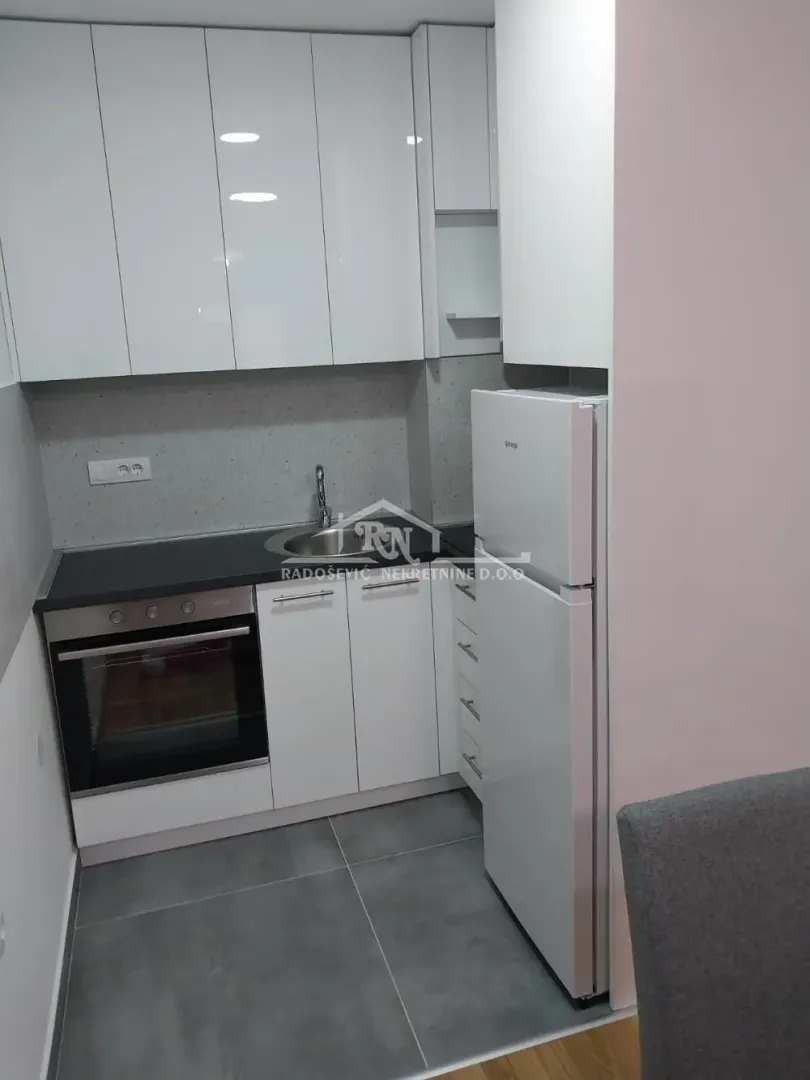 Manja bela kuhinja sa ugrađenom rernom, sudoperom i frižiderom.