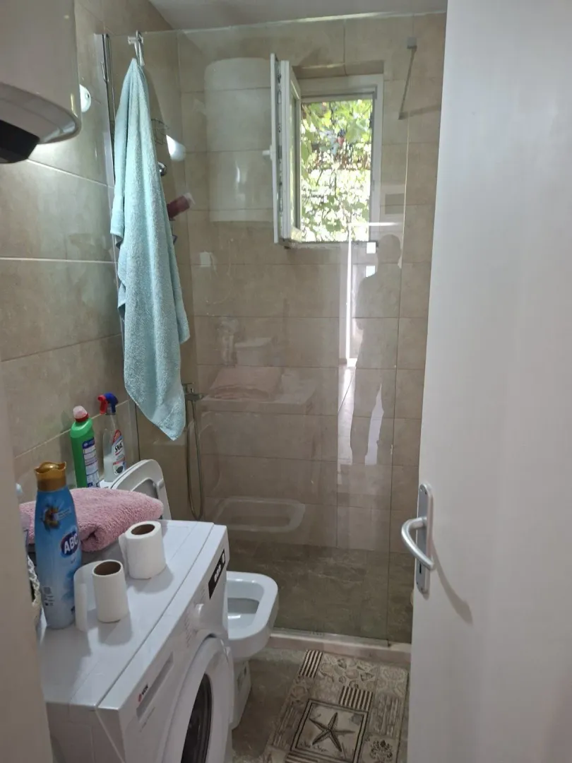 A bathroom with a walk-in shower, washing machine, and a window.