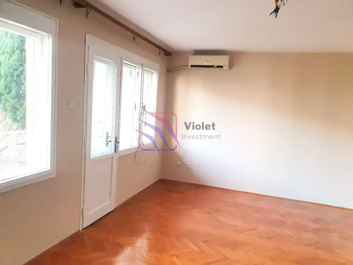 Prazna soba sa parketom na podu i klima uređajem na zidu.