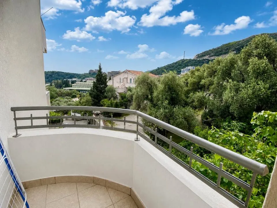 Manji polukružni balkon sa metalnom ogradom i pogledom na zelenilo i okolne zgrade.