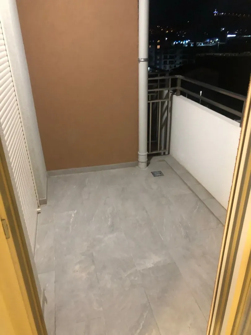 Prazna natkrivena terasa sa keramičkim pločicama i pogledom na grad noću.
