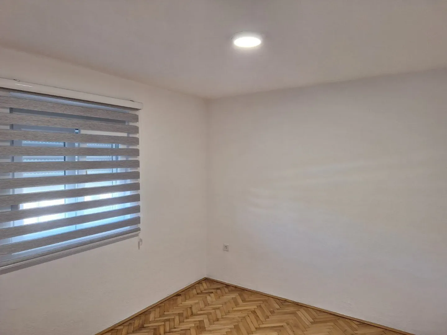 An empty room with parquet flooring and window blinds.