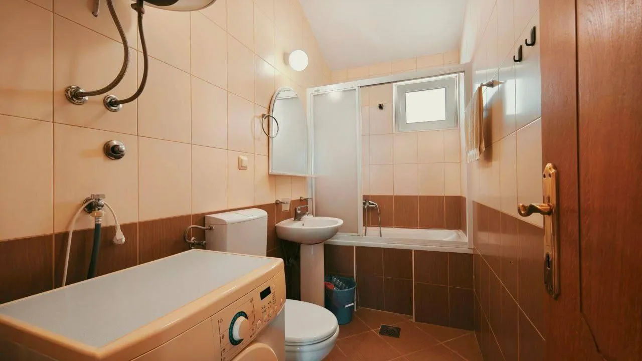 Small bathroom with ceramic tiles, washbasin, toilet bowl, and bathtub.