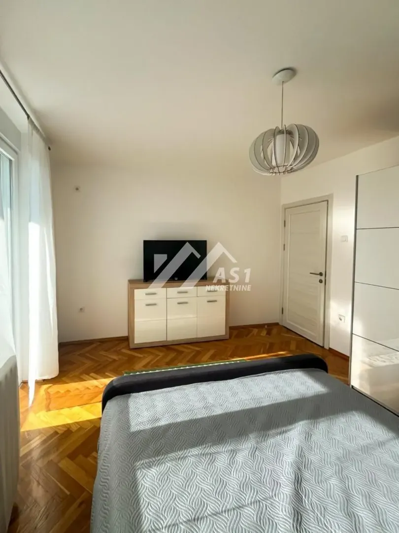 Nameštena spavaća soba sa bračnim krevetom, komodom i televizorom.