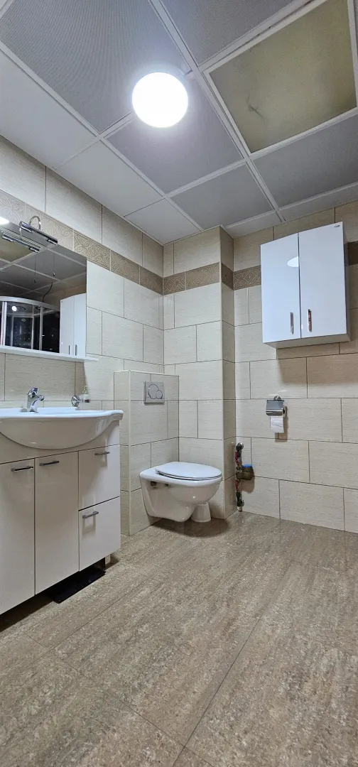 Potpuno opremljeno kupatilo sa svijetlim pločicama, umivaonikom i toaletom.